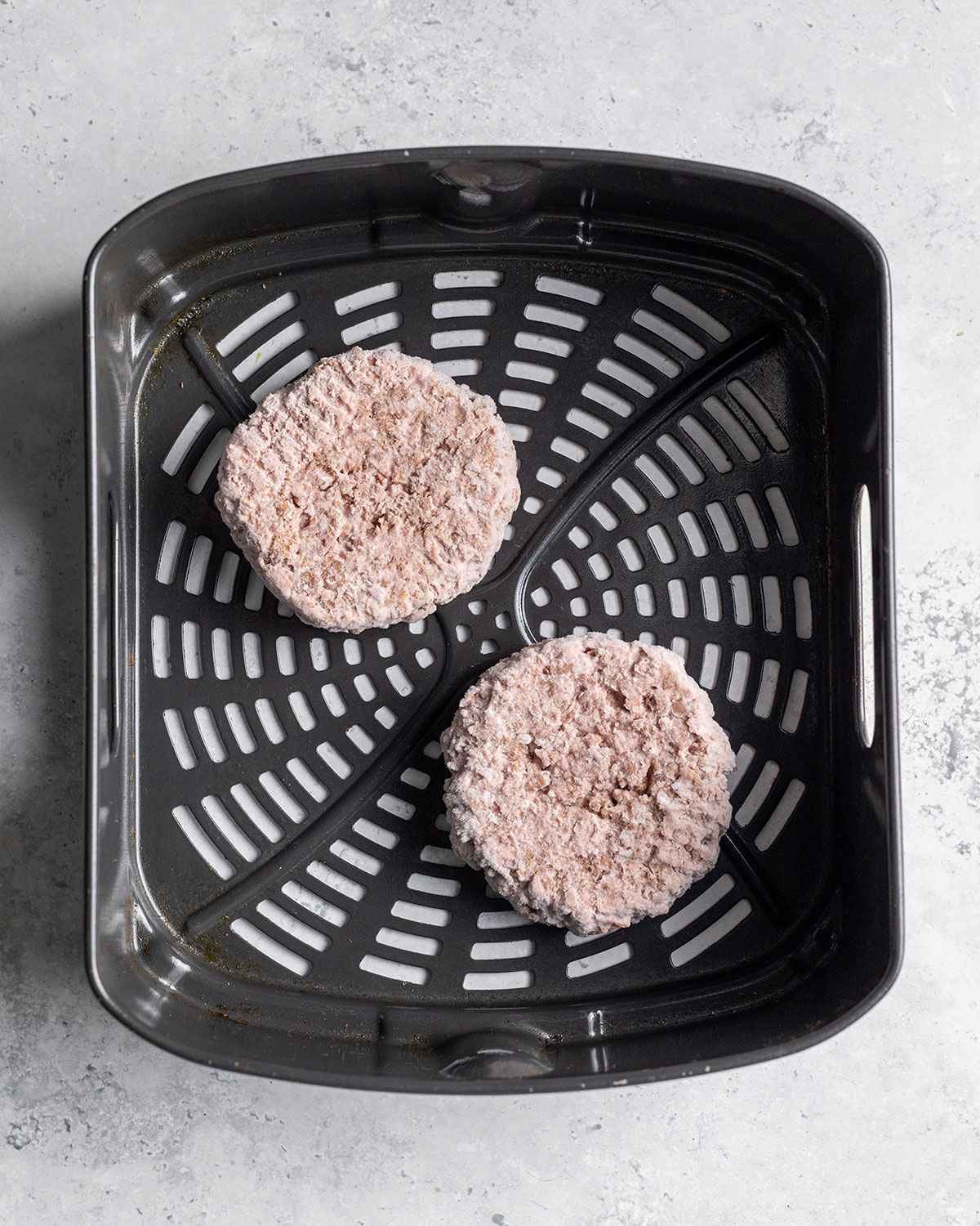 two frozen burgers in air fryer basket