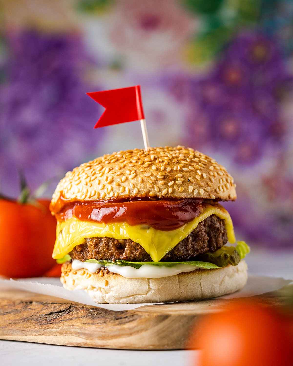 A homemade vegan cheeseburger sitting on a wooden serving tray with a small red flat on top of the seeded burger bun.