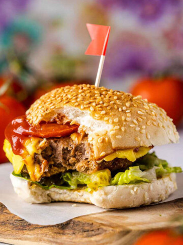 an air fryer frozen burger sitting on a woodden serving board with a bite taken out of it