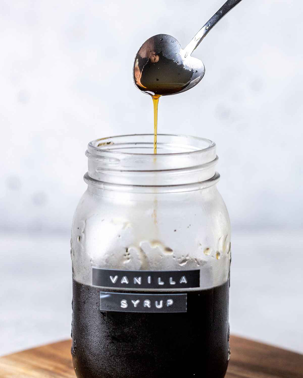 a spoon drizzling vanilla syrup into a glass jar