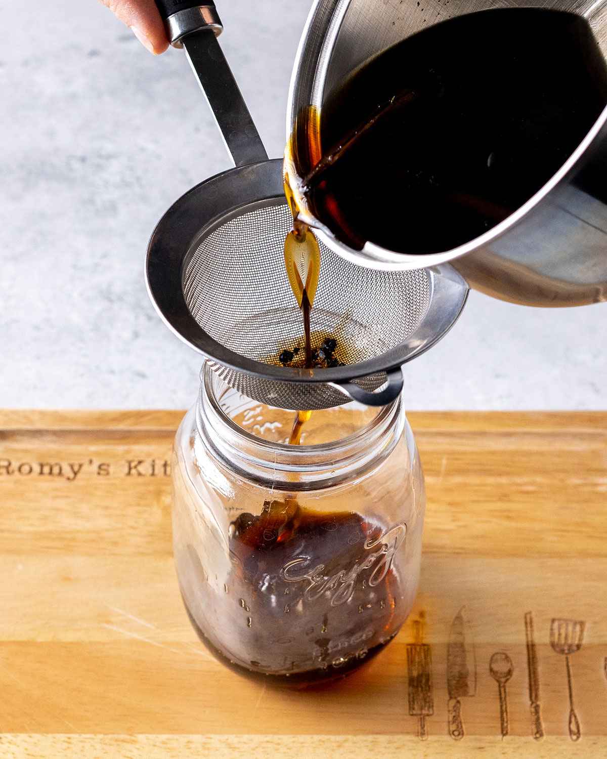 coffee syrup being strained through a sieve into a glass jar