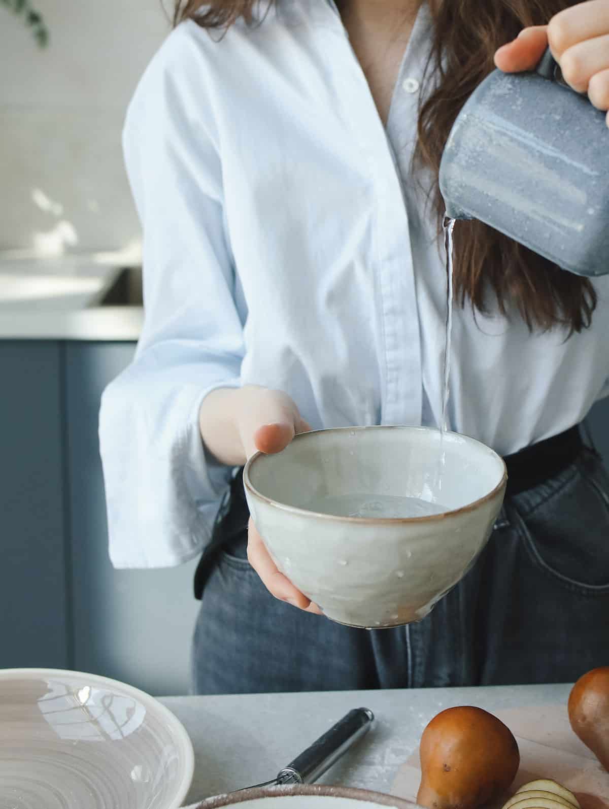 A hand pouring water into a ceramic bowl in the kitchen.