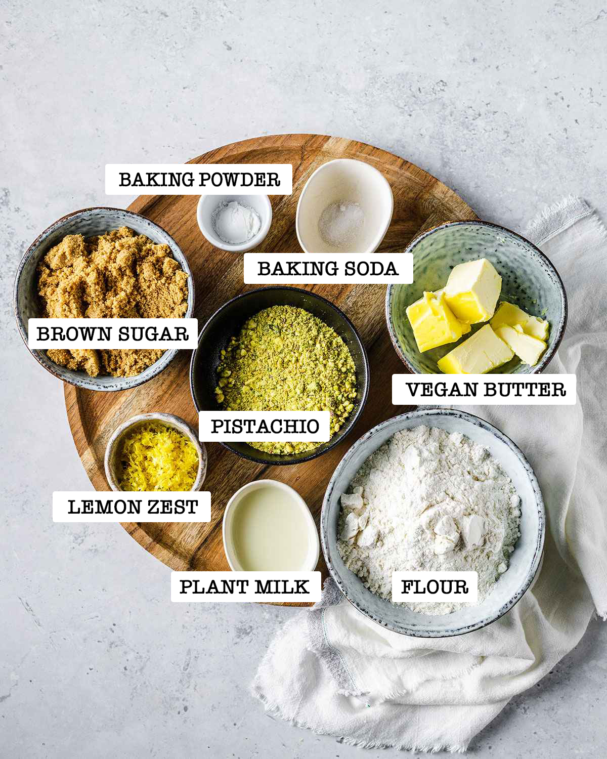 Measured ingredients for pistachio cookies in small bowls with labels.