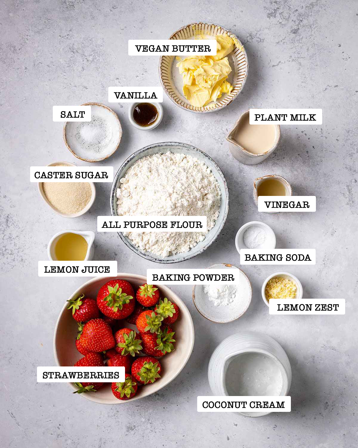 all ingredients for vegan strawberry shortcake on a white marble table with labels