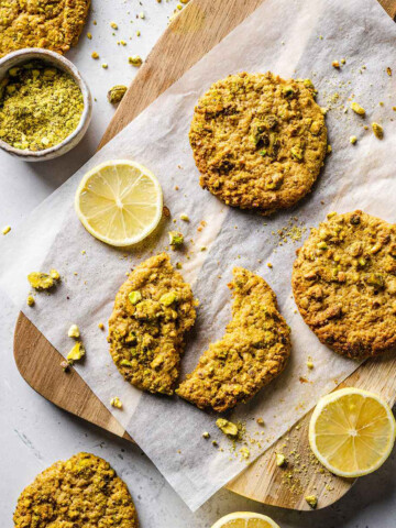 Pistachio cookies on a parchment paper, with one cookie broken in half.