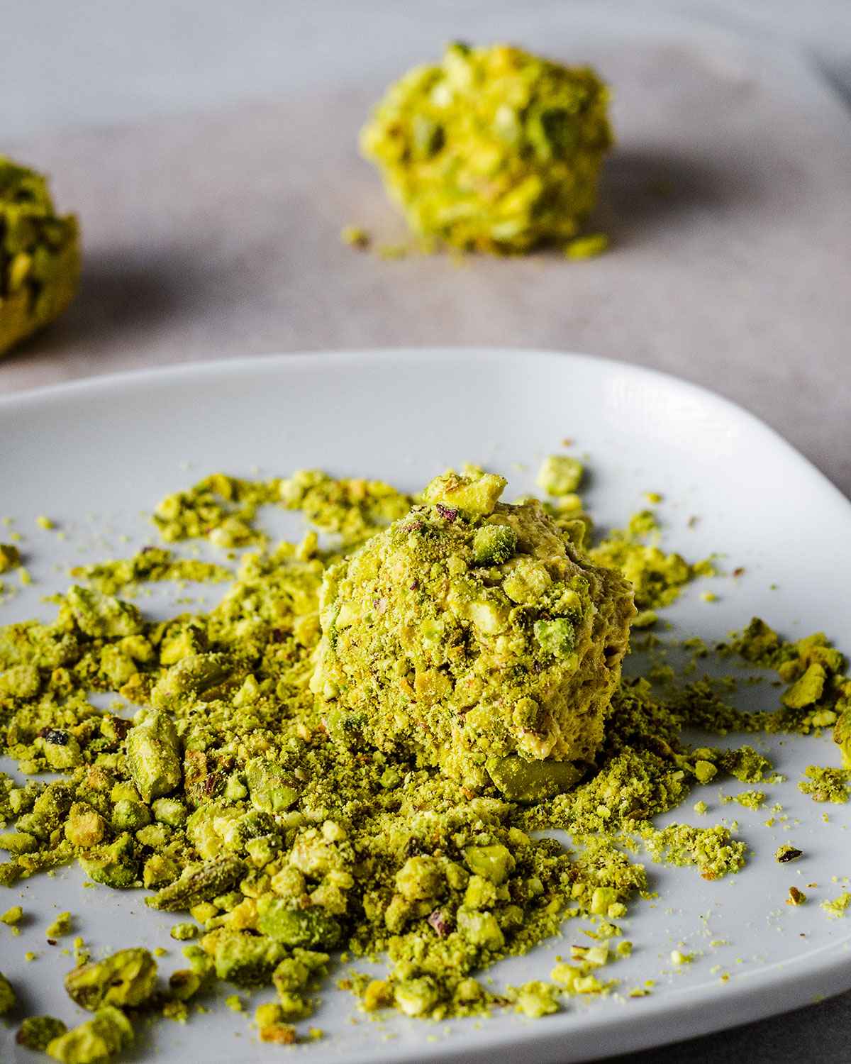 Cookie dough ball rolled in crushed pistachios on a small plate.