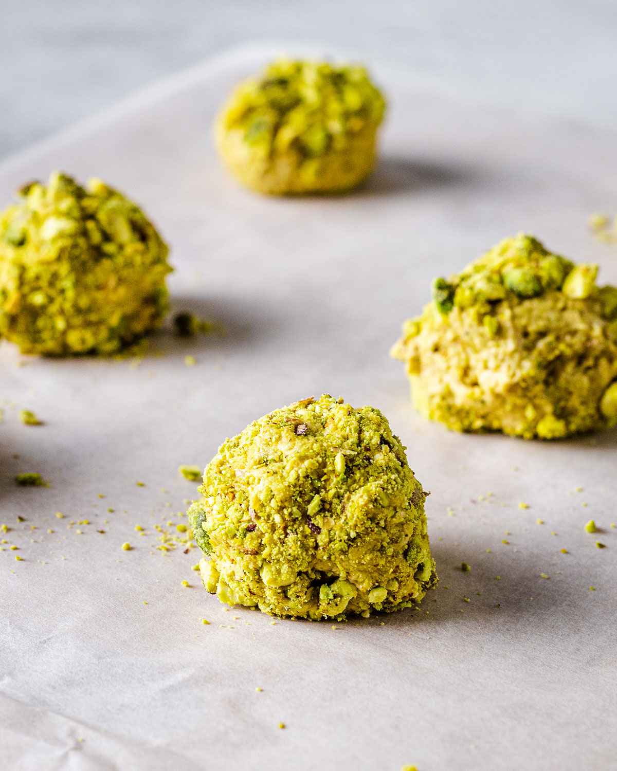 Cookie dough balls coated in pistachio nuts on a baking sheet. 