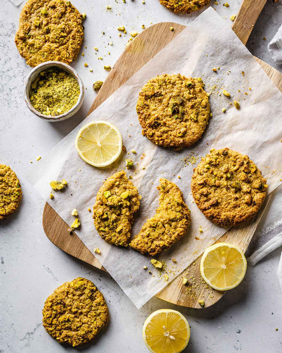 Multiple pistachio cookies on a parchment paper after baking with one cookie broken in half.