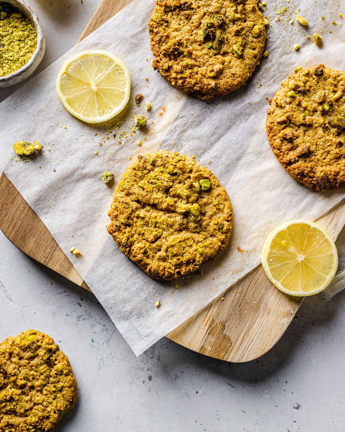 Vegan pistachio cookies on a parchment paper next to lemon slices.