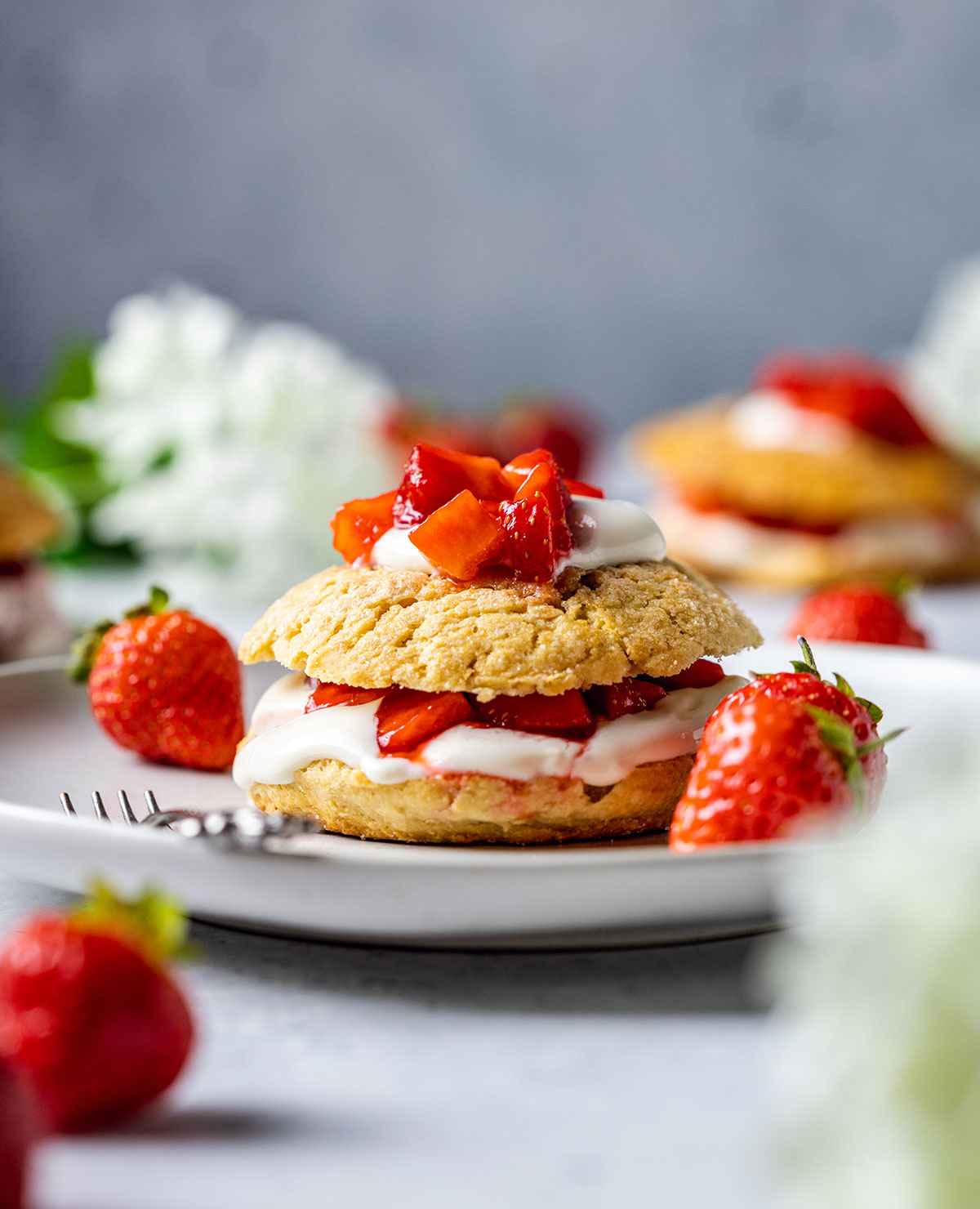 vegan strawberry shortcake topped with vegan coconut cream and strawberries on a white plate