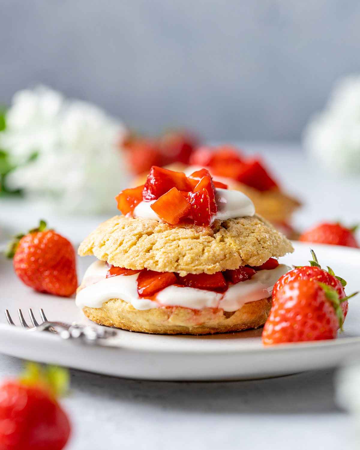 vegan strawberry shortcake topped with vegan coconut cream and strawberries on a white plate