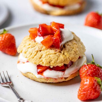 vegan strawberry shortcake topped with vegan coconut cream and strawberries on a white plate with a small fork on the side