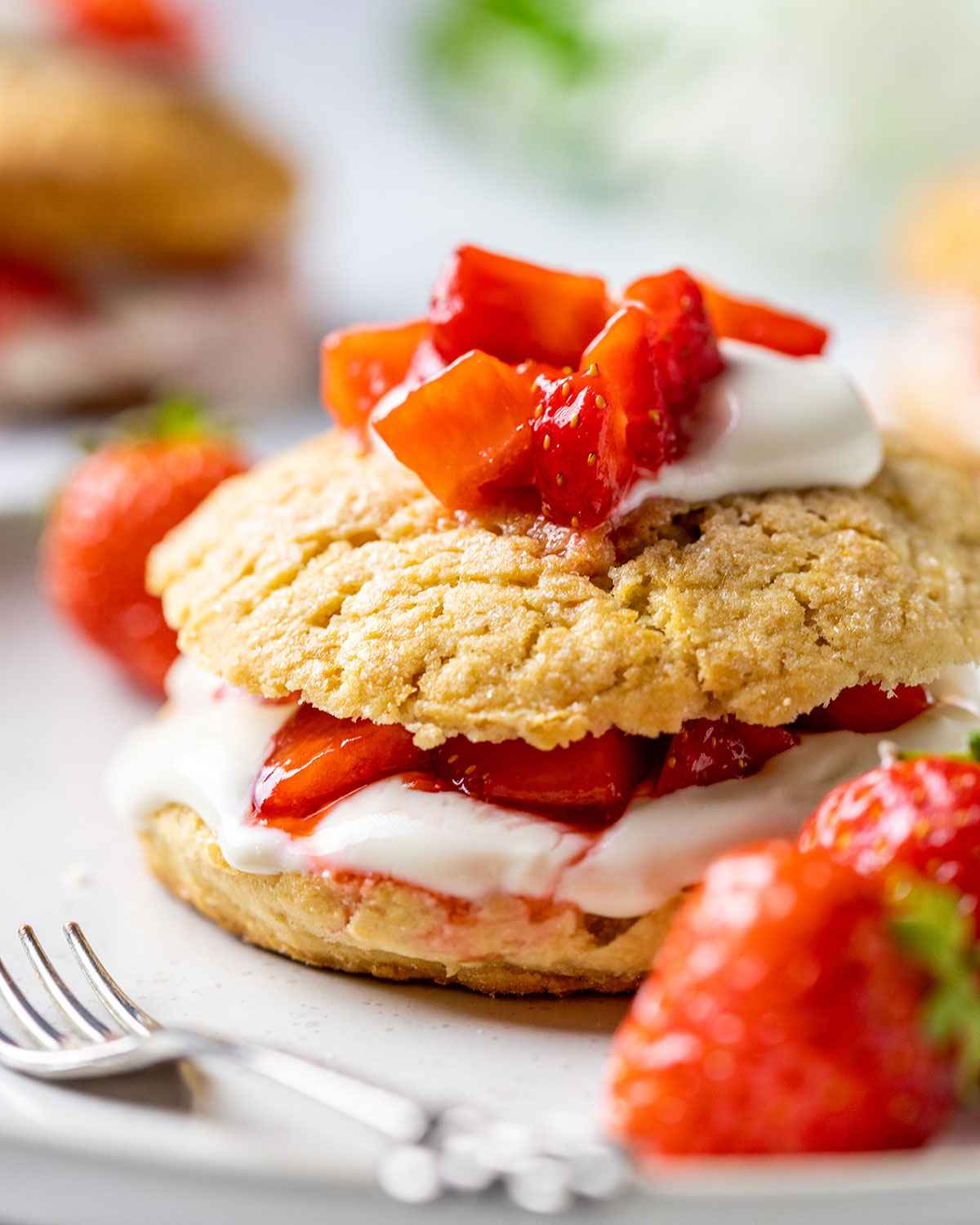 vegan strawberry shortcake topped with vegan coconut cream and strawberries on a white plate and a tiny fork next to it