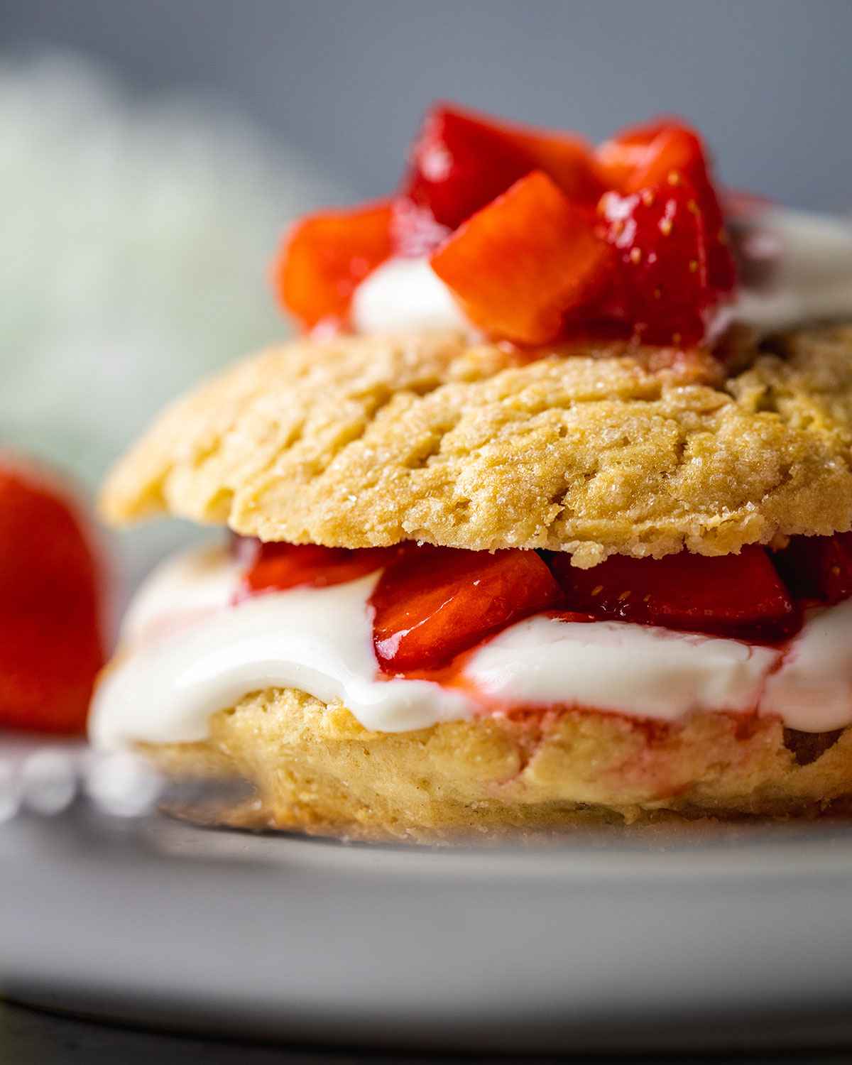 close up of vegan strawberry shortcake topped with vegan coconut cream and strawberries on a white plate