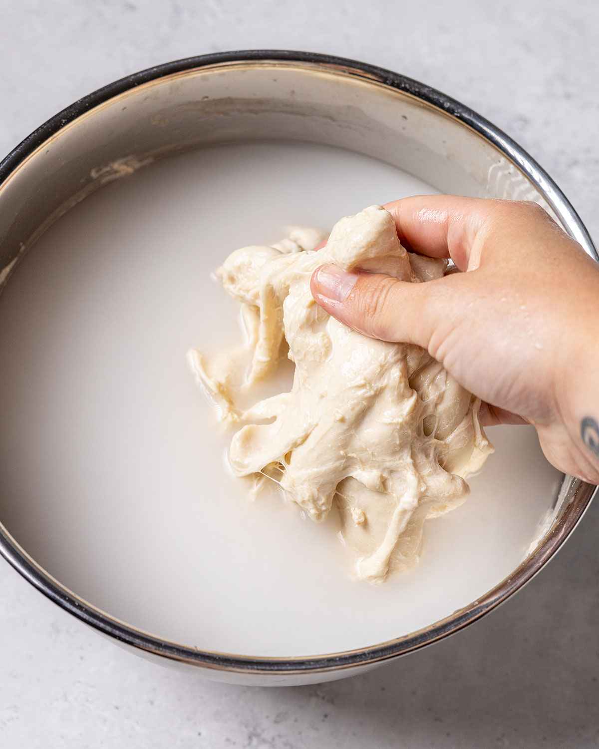 a hand washing a flour ball in a bowl full of water. The flour ball looks like it's softening and the water has turned white