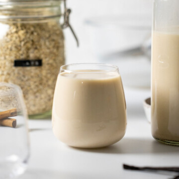 a full glass of easy homemade oat milk, surrounded by ingredients