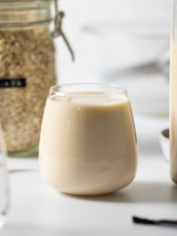 a full glass of easy homemade oat milk, surrounded by ingredients