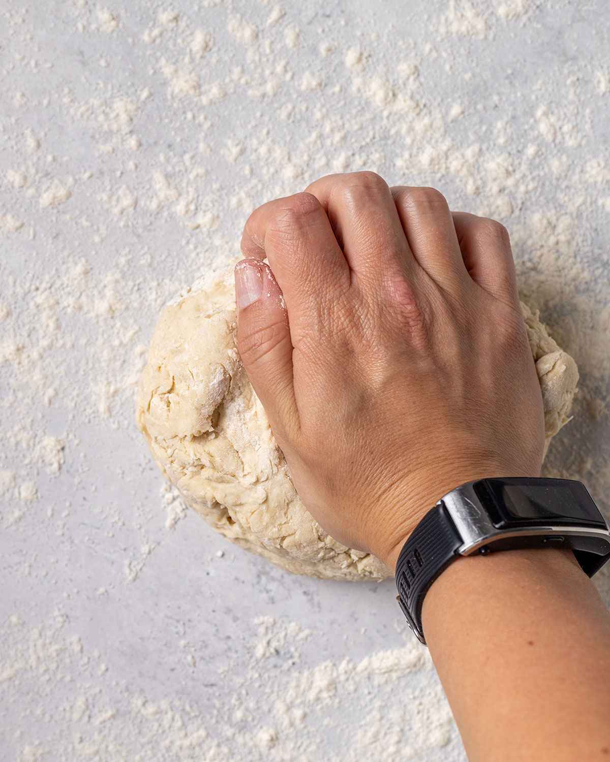 a hand kneading a dough ball on a floured marble surface