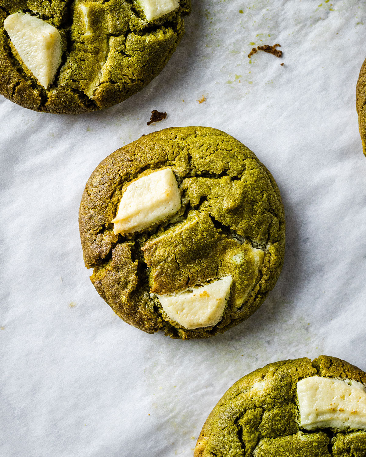 Matcha green tea cookies with white chocolate chips on a white baking parchment