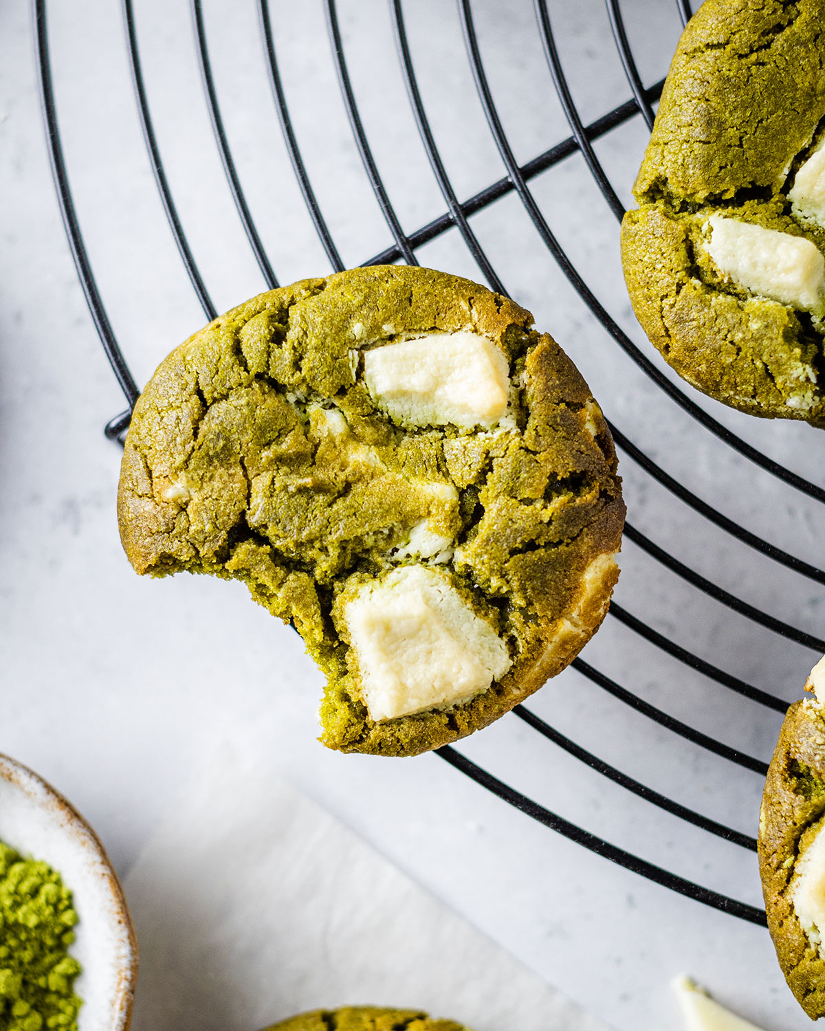 matcha cookie with white chocolate and a bite taken out of it placed on a cooling rack