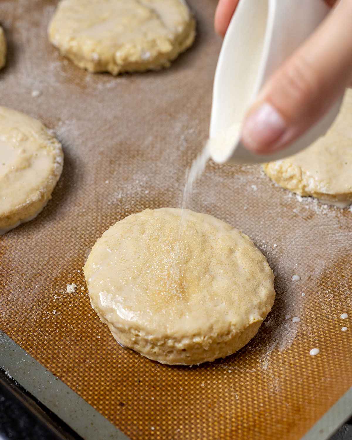 sprinkling caster sugar onto vegan shortcake sitting on a baking tray