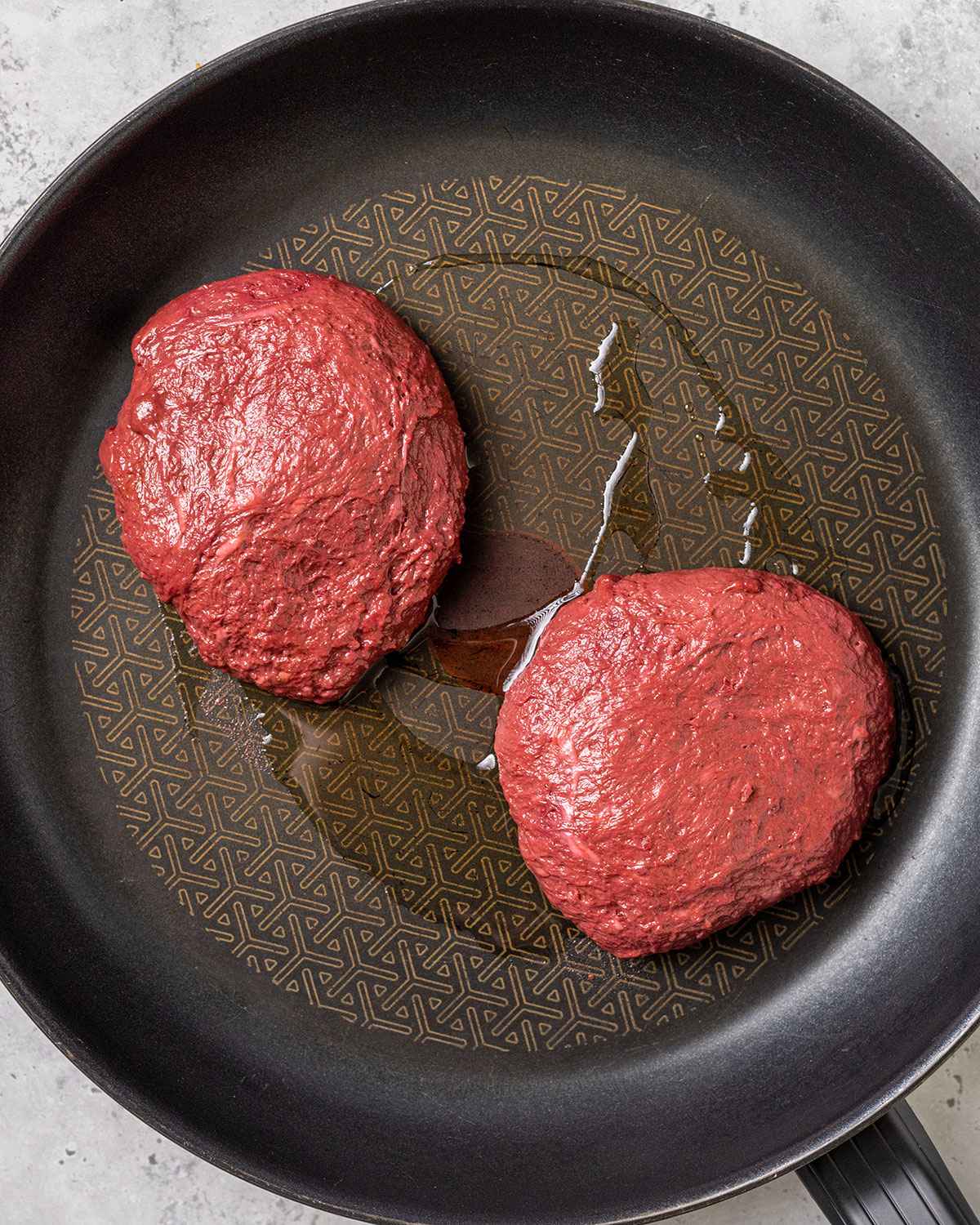 two uncooked seitan steaks in a skillet with a little oil