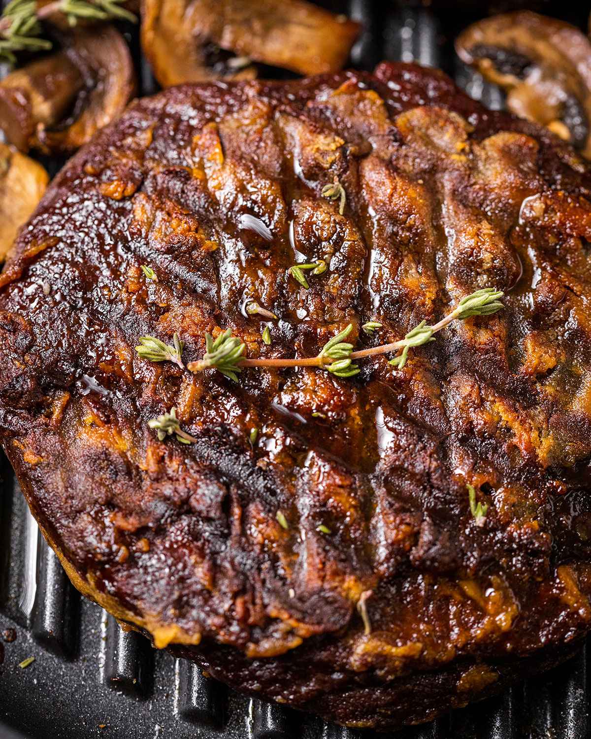 close up of a vegan steak in a skillet with mushrooms, thyme, garlic and roasted potato cubes