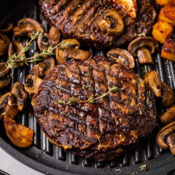 two vegan steaks in a skillet with mushrooms, thyme, garlic and roasted potato cubes