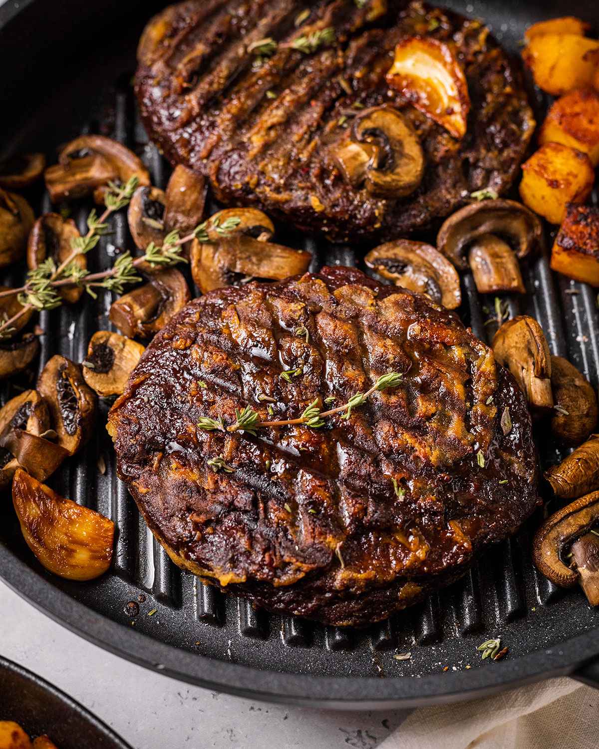 two vegan steaks in a skillet with mushrooms, thyme, garlic and roasted potato cubes