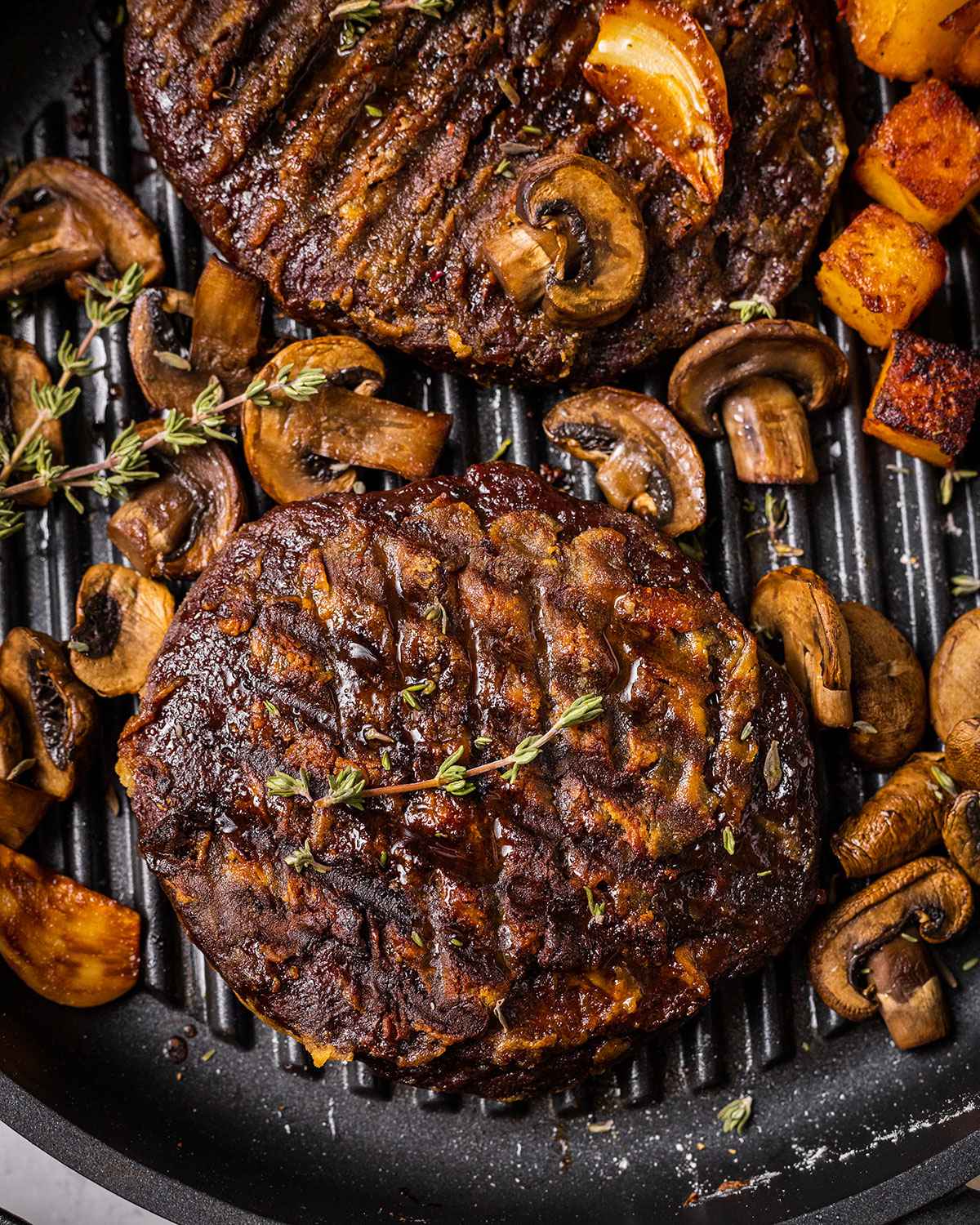 two vegan steaks in a skillet with mushrooms, thyme, garlic and roasted potato cubes