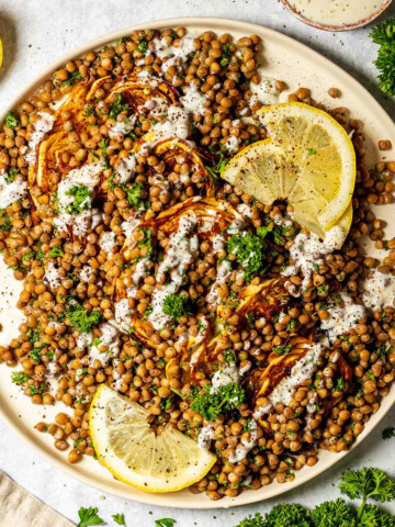 roasted cabbage steaks and lentil salad on a white serving platter on a marble table surrounded by ingredients