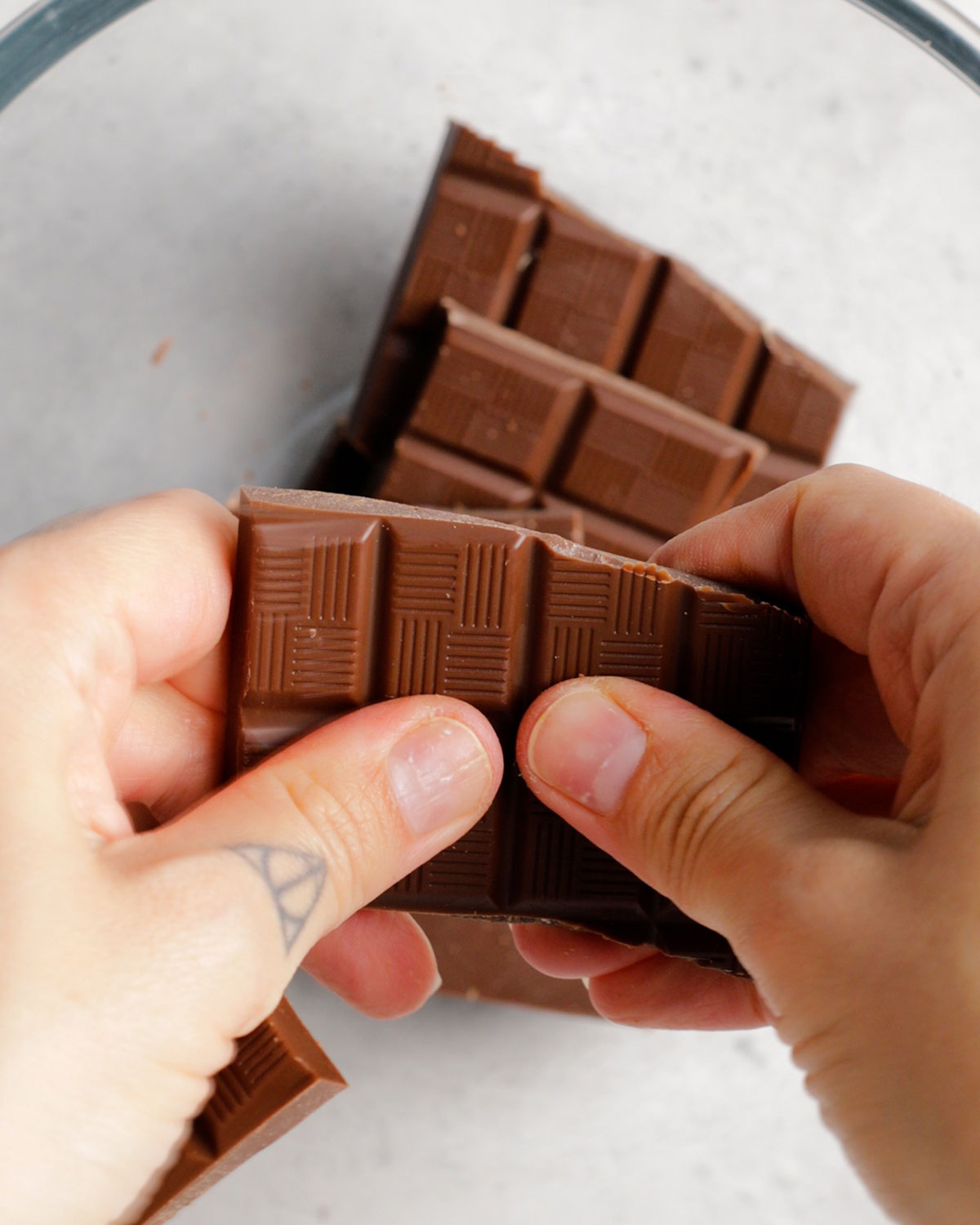 two hands breaking vegan chocolate into a glass bowl