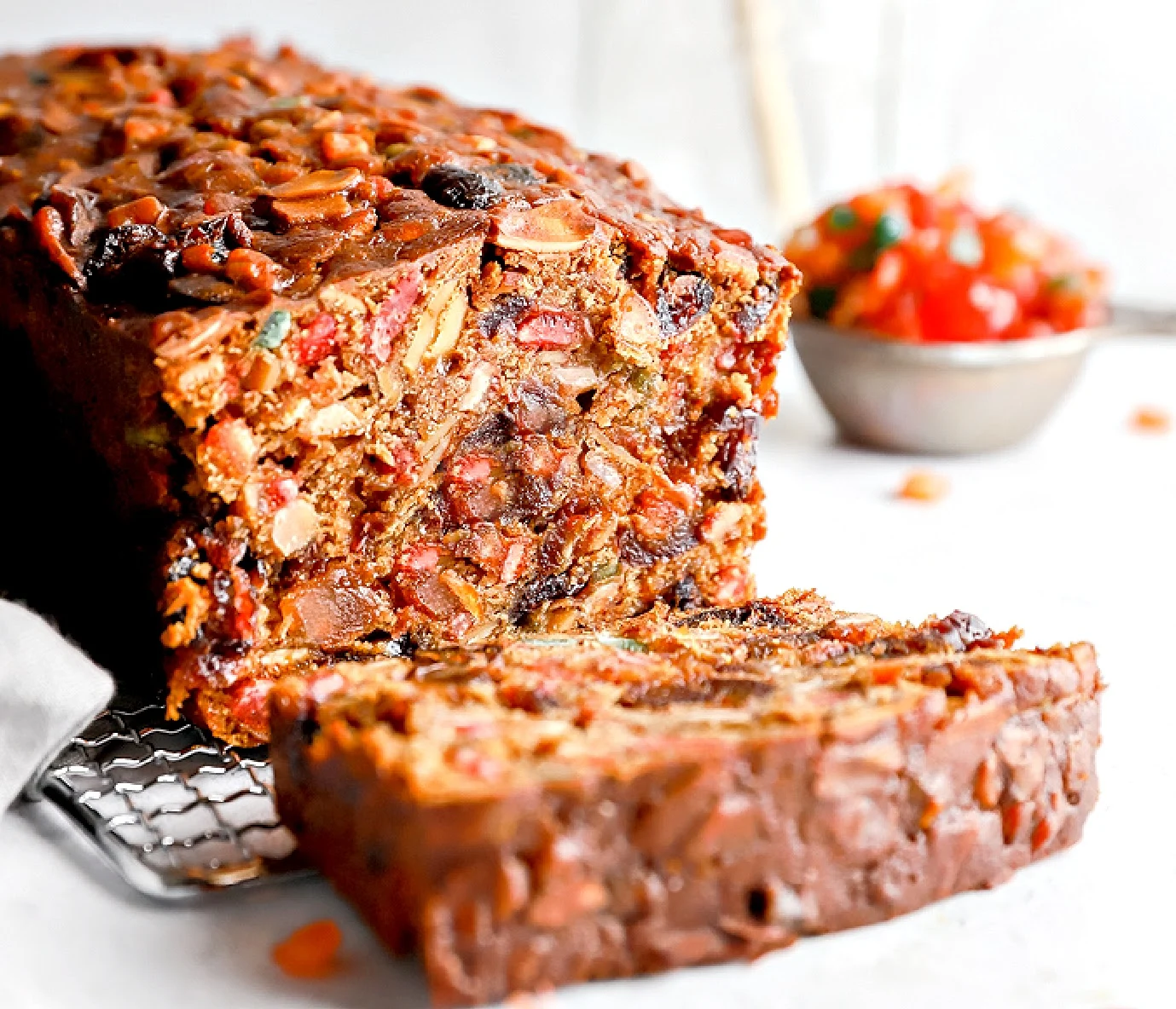 a loaf shaped Christmas fruit cake on a cooling rack with a slice cut at the front exposing the nuts and seeds in the fruit cake