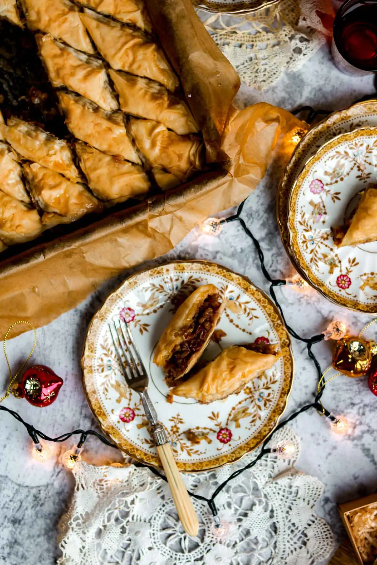 Vegan mince pie baklava on a sheet pan with a few pieces of vegan baklava on a small plate with a fork next to it. The entire scene is decorated with fairy lights and a festive tablecloth