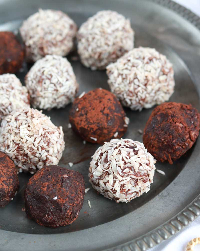 a plate filled with vegan rum balls, some coated with coconut shreds, others dusted with cacao powder.