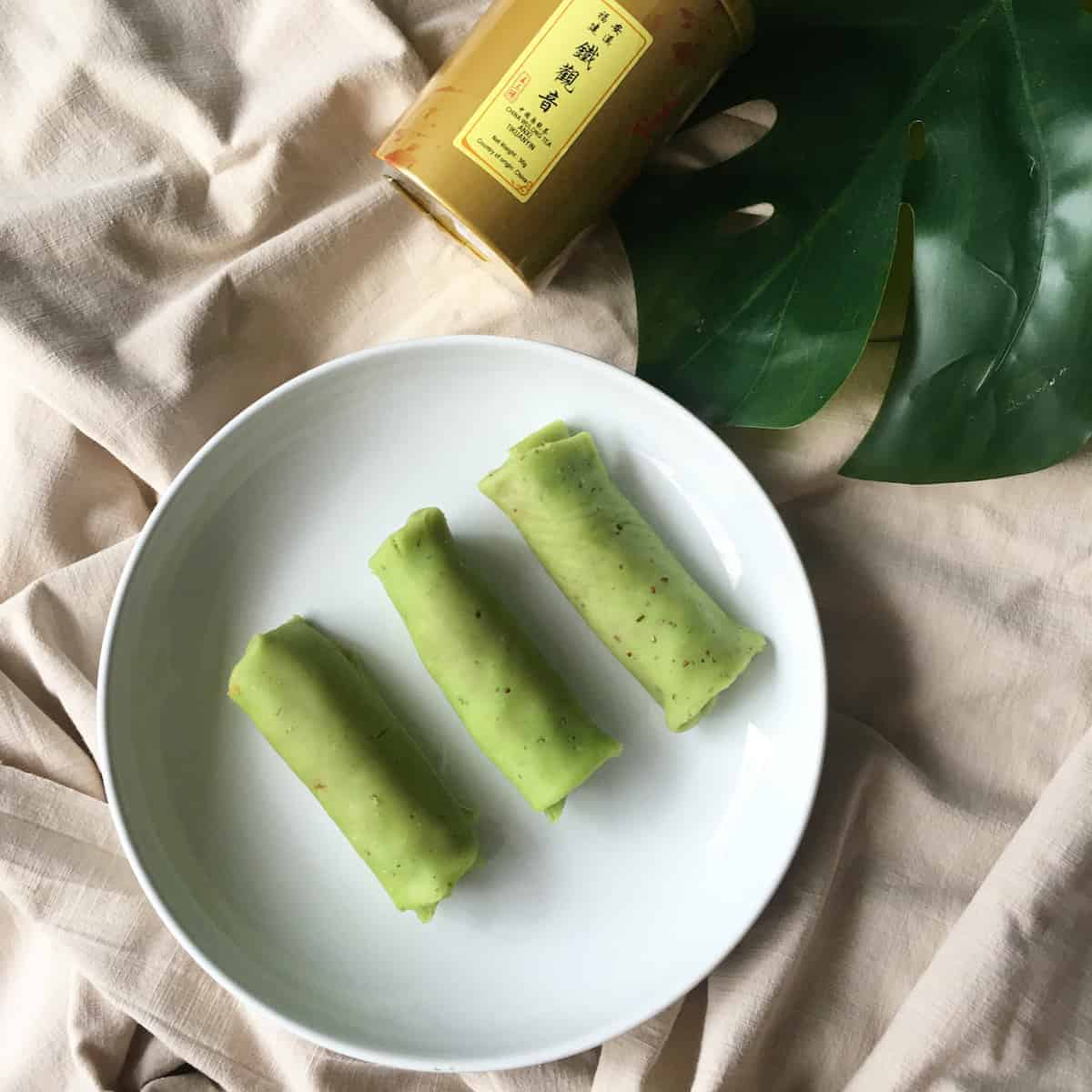 3 kueh dadar pandan coconut pancakes, rolled upon a white plate placed on a tablecloth