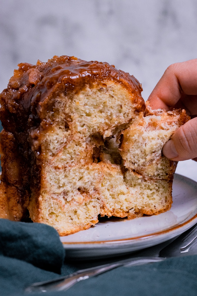 a slice of vegan monkey bread on a white plate, a hand coming in from the right and ripping a piece of the monkey bread