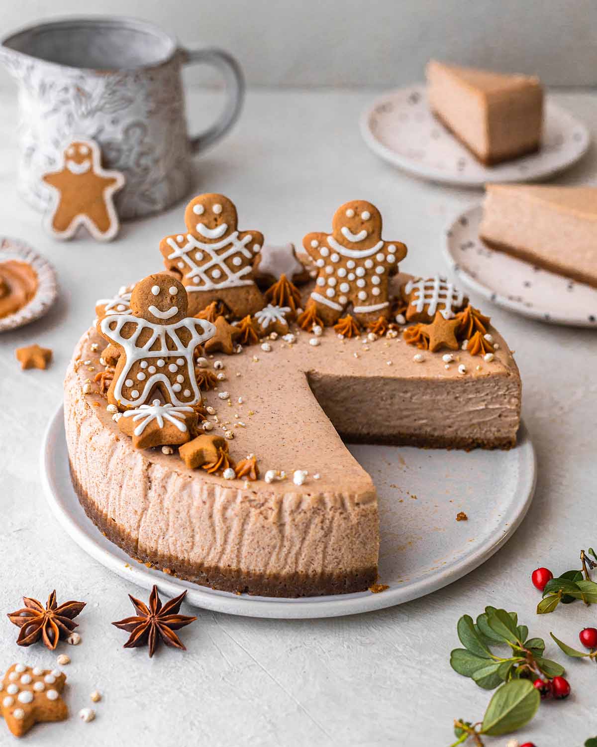 a round vegan gingerbread cheesecake, decorated with 3 vegan gingerbread men on top on a white platter with 2 slices cut out of it