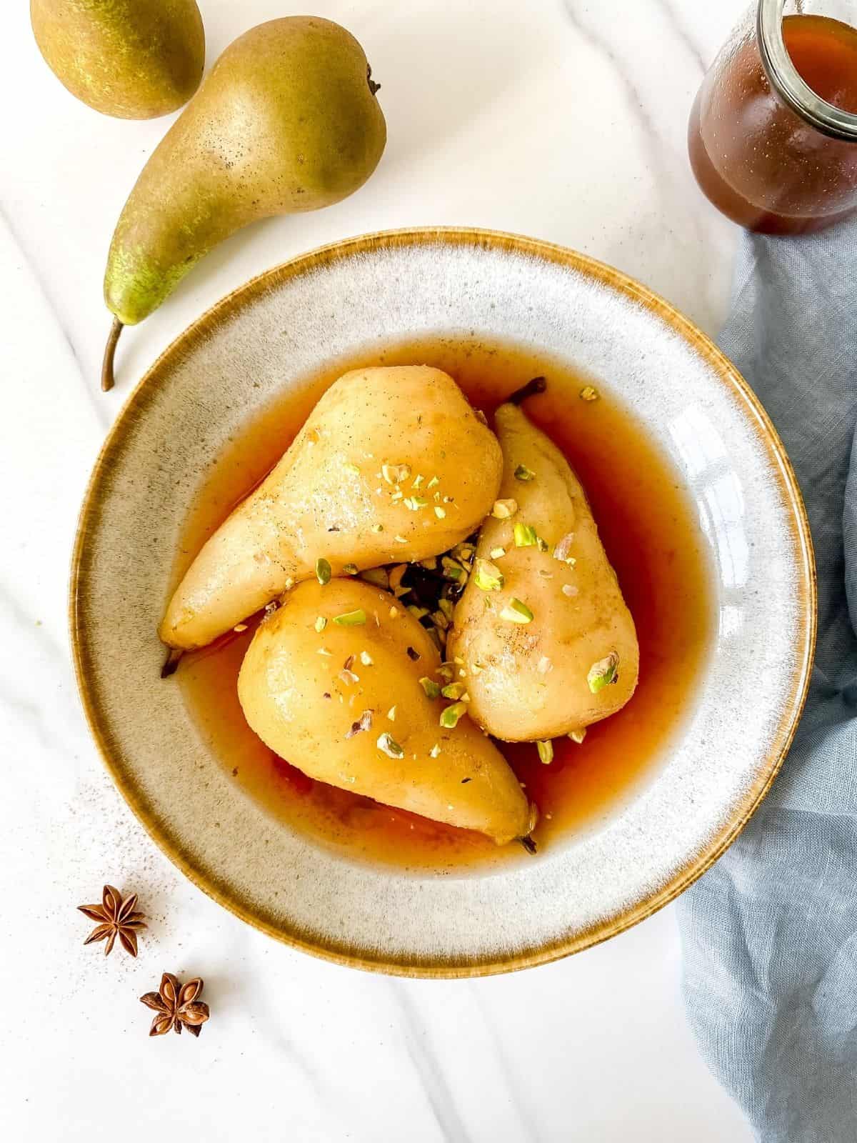 3 spiced poached pears in a white bowl as seen from above.