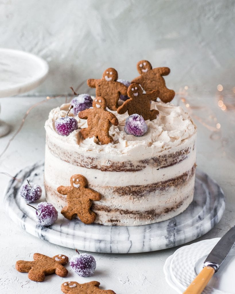 vegan gingerbread cake with three layers on a white table with vegan gingerbread men on top