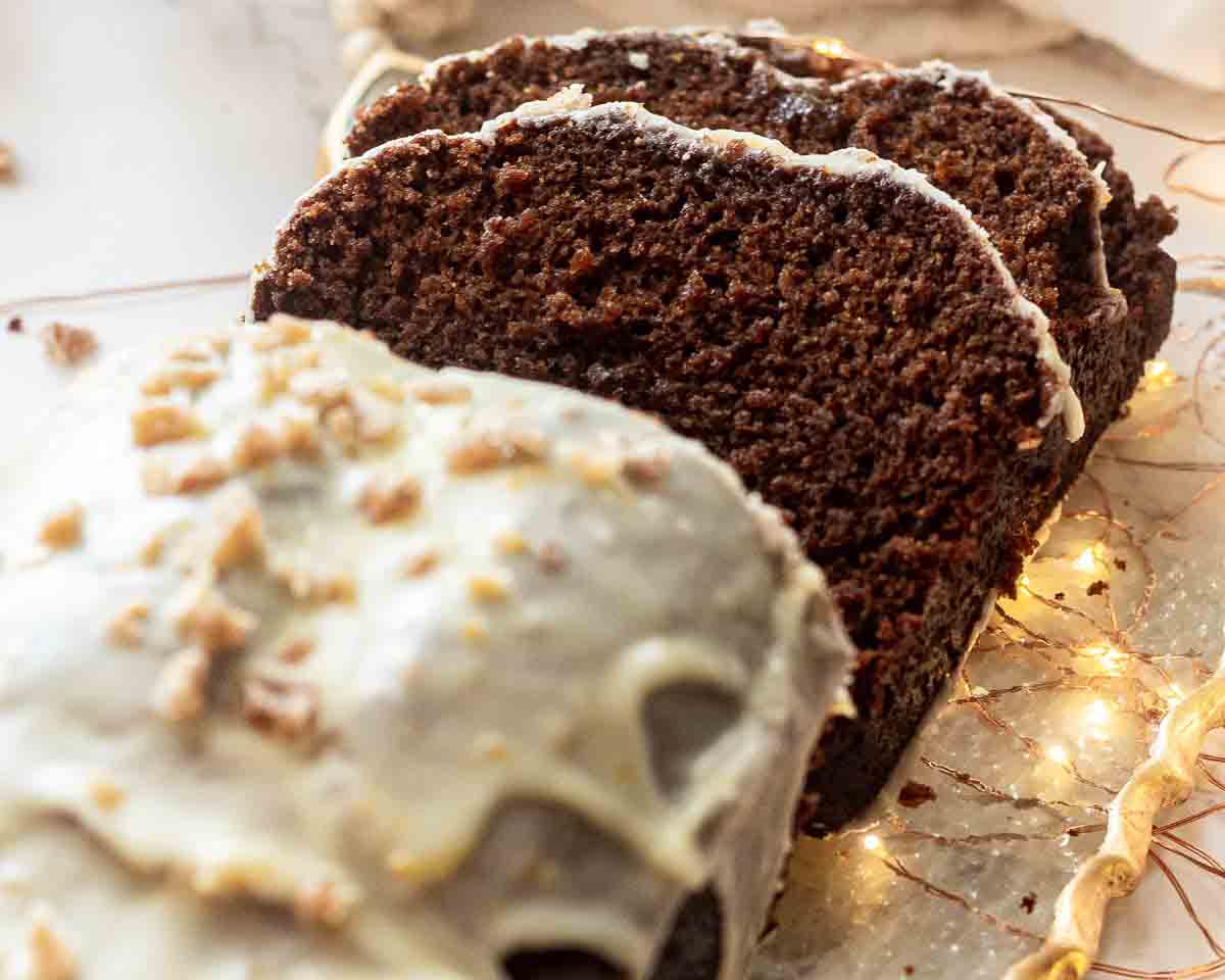 vegan gingerbread loaf cake with white frosting on top, a few slices are cut showing the fluffy inside of the festive loaf cake