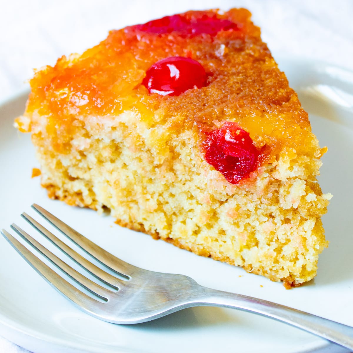 a slice of vegan pineapple upside down cake on a white plate with a fork next to it