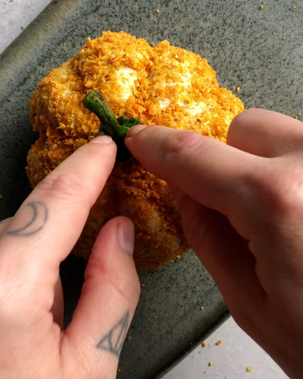 2 fingers attaching a bell pepper stem on top of a pumpkin shaped cheese ball