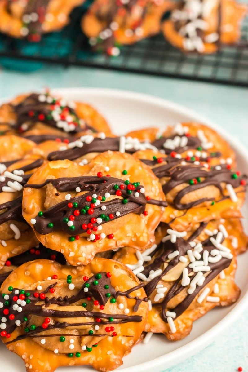 a white plate with piled pretzel bites. the bites are topped with peanut butter, vegan chocolate and festive sprinkles.