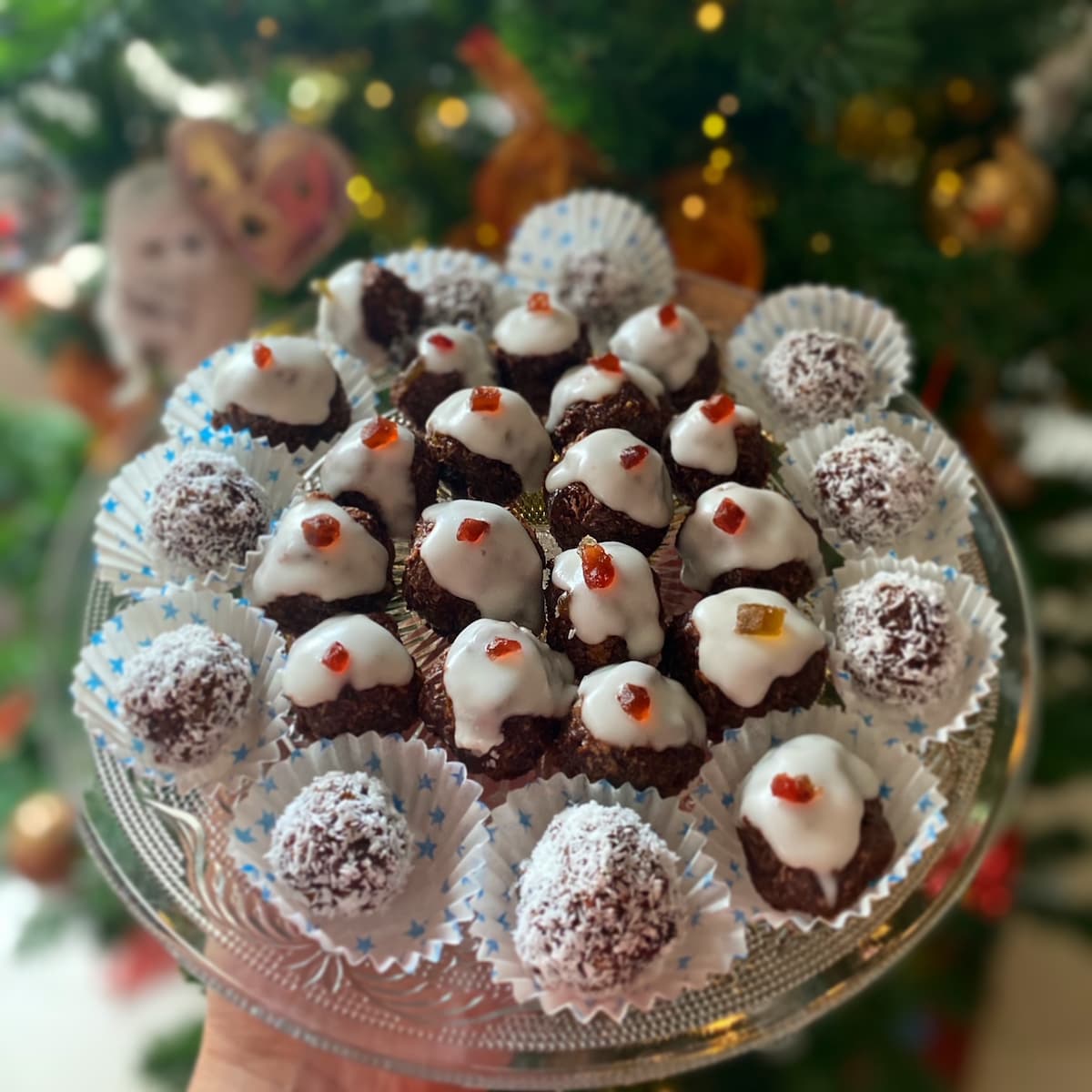 a round plate held by a hand filled with vegan chocolate truffles decorated as christmas puddings and snow balls
