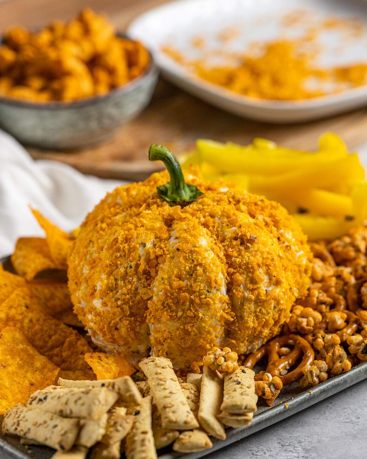 a pumpkin shaped cheese ball on a serving tray surrounded by different kind of nibbles