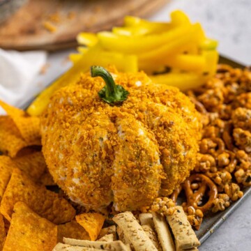 a pumpkin cheese ball on a serving board surrounded by crackers