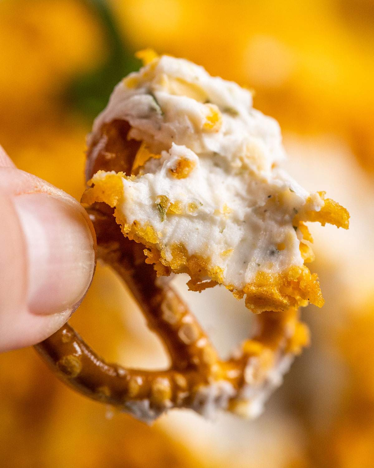 a crunchy pretzel, held by a hand with vegan cream cheese on the pretzel