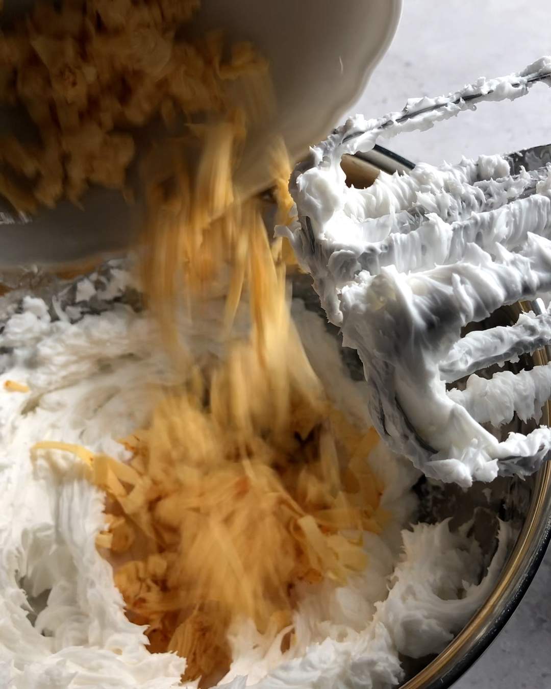 Shredded being added to a bowl full of whipped vegan cream cheese