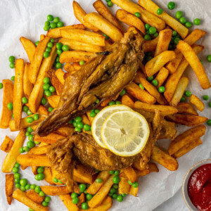 vegan banana blossom dish on a serving of french fries with peas and lemon slices, as seen from above